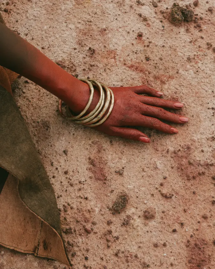 Hand with gold bangles on red earth